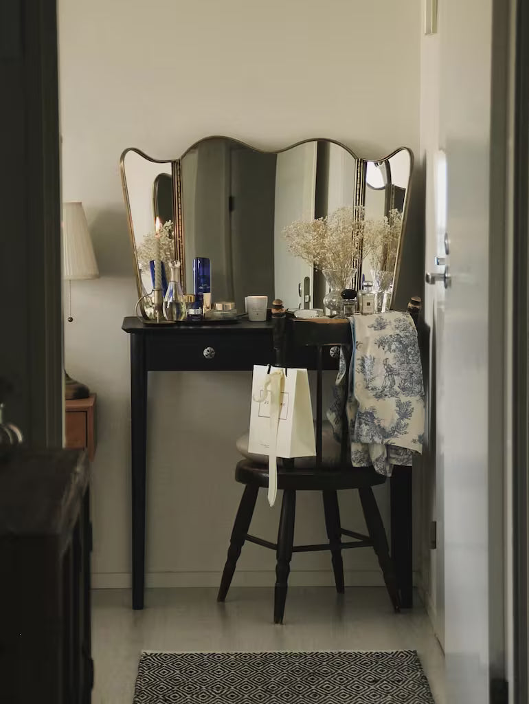 Espejo de tres hojas con acabado en latón envejecido sobre cómoda con flores y lámparas de aceite. Estilo vintage elegante y artesanal.